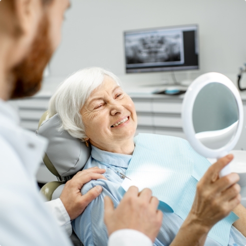 Senior dental patient looking at her smile in mirror