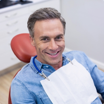 Man in denim shirt smiling in dental chair