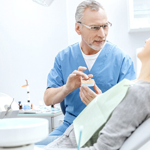 a dentist talking with his patient while holding a model jaw