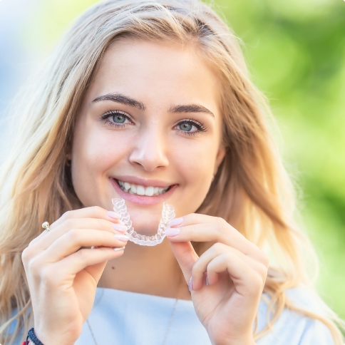 Smiling blonde woman holding Invisalign clear aligner