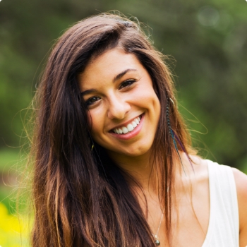 Young woman with long brown hair grinning outdoors