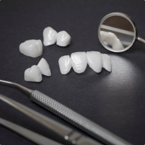 Several dental crowns and veneers on table with dental instruments