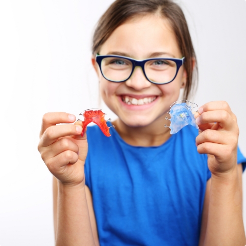 Smiling young girl holding an orthodontic retainer in each hand