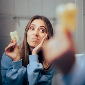 Woman holding her cheek in one hand and a fake tooth in the other