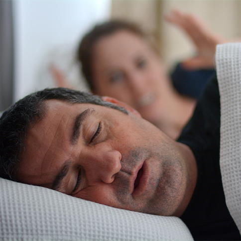 Frustrated woman lying in bed next to snoring man