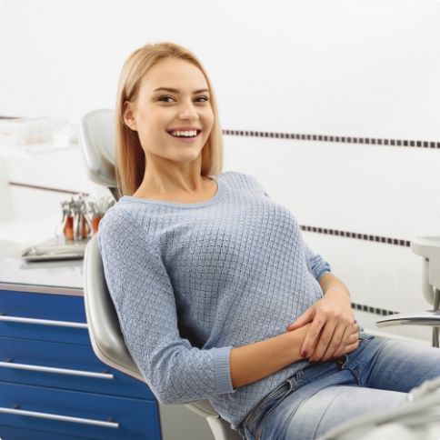 Smiling young woman in blue sweater sitting in dental chair