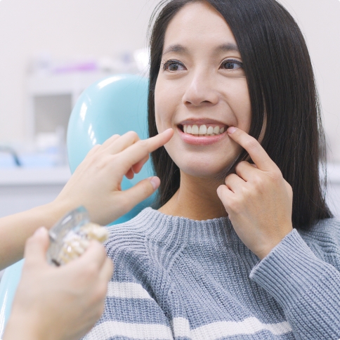 Woman in dental chair pointing to her smile