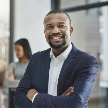 Man in business attire standing and smiling with arms crossed