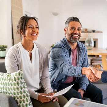 Man on couch shaking hands with someone sitting across from him