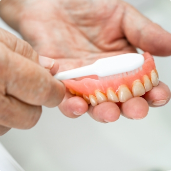 Person cleaning their denture with a toothbrush