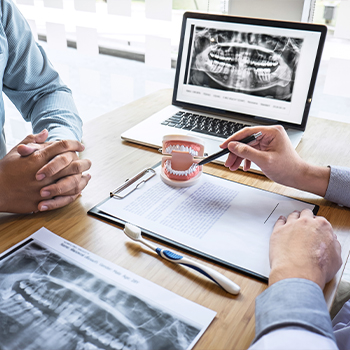 Dentist talking with patient next to computer screen showing x rays of teeth