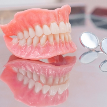 Full dentures resting on table next to two dental mirrors