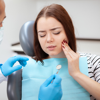 Woman holding her cheek in pain while talking to her dentist