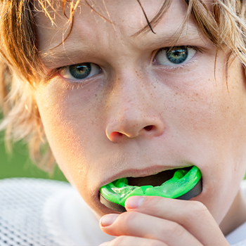 Child placing a green mouthguard over his teeth