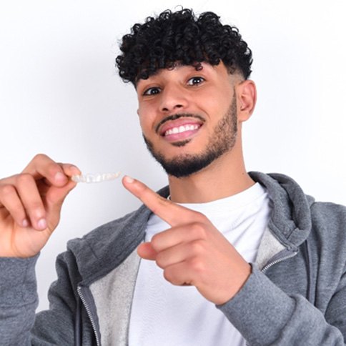 smiling man pointing at an Invisalign aligner