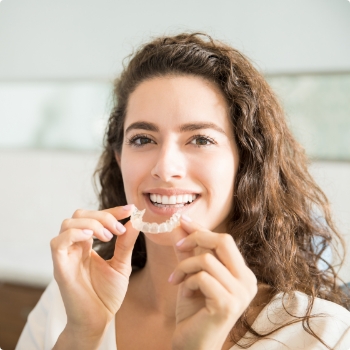 Woman with curly brown hair holding an Invisalign tray