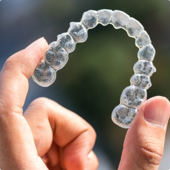 Hand holding an Invisalign aligner outdoors