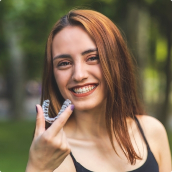 Smiling brunette woman holding an Invisalign aligner outdoors
