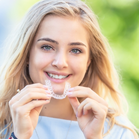 Smiling blonde woman holding an Invisalign clear aligner