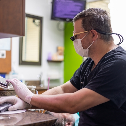 Doctor Mulkey wearing dental binoculars and mask while typing on computer