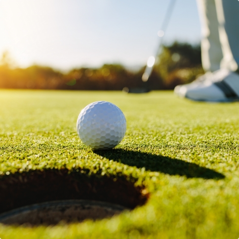 Golf ball right next to hole with golfer in background