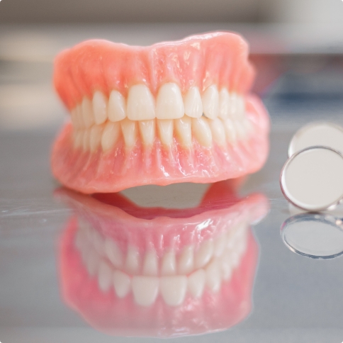 Set of full dentures resting on table next to two dental mirrors