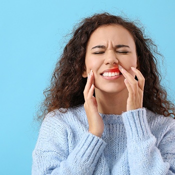 Woman in blue sweater touching her red inflamed gums with eyes closed in pain