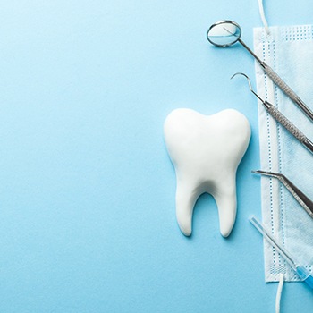Model tooth next to dental instruments and mask with light blue background