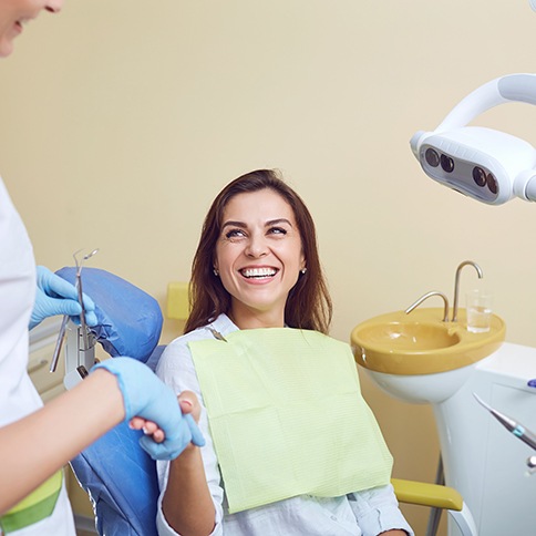 Smiling dental patient shaking hands with her dentist