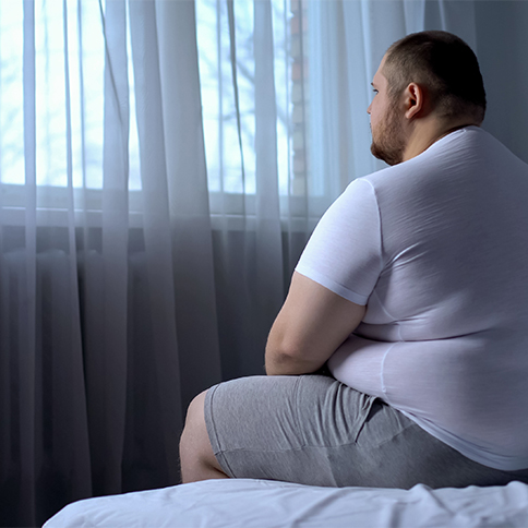 Large man sitting on bed needing sleep apnea treatment in Weatherford