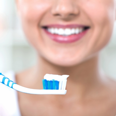 Smiling person holding toothbrush with dab of toothpaste on it