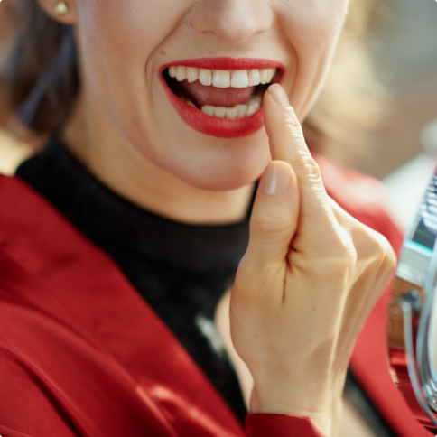 Woman with red lipstick looking at her smile in mirror