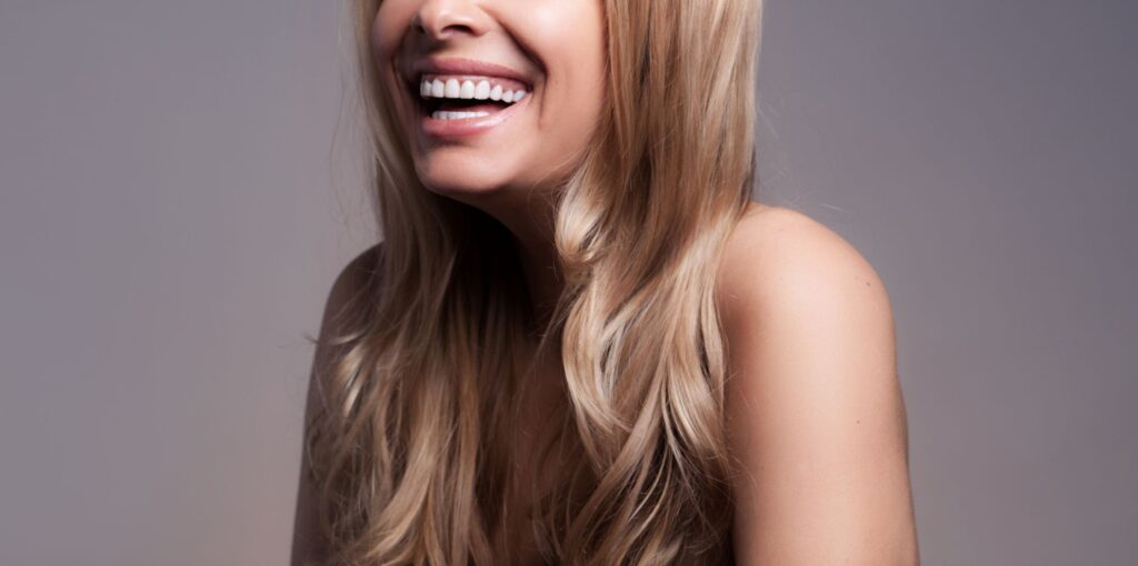 Nose to chest view of blond woman with perfect teeth smiling