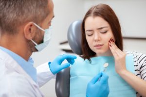 a young woman holding her cheek in pain while waiting to hear from the dentist